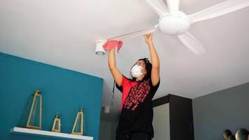 A person cleaning a ceiling fan in a room with teal walls and a white ceiling.