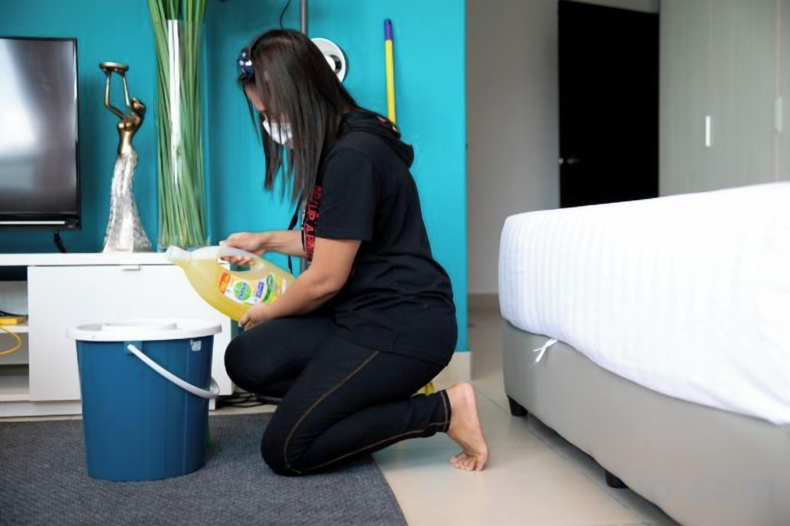 A person sitting on the floor in a room with a bed, a desk, and a television.