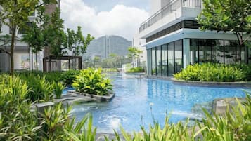 A swimming pool with surrounding greenery, a modern building with balconies, and a mountain in the background.