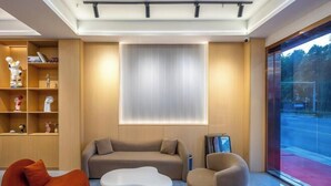 A modern living room with a sofa, a white coffee table, and a red chair. There is a bookshelf with decorative items and a window with blinds. - Yimi Hotel (Provincial Library Branch near Hainan Institute of Business and Technology) (Haikou)