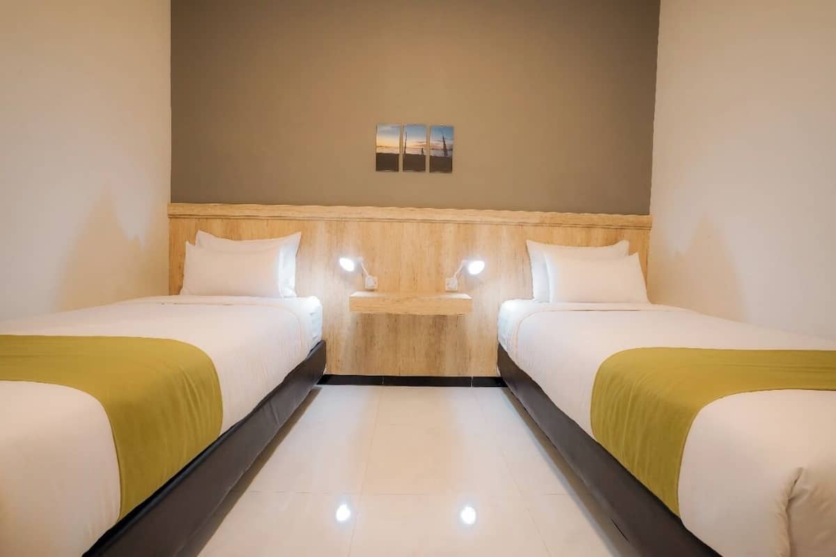 A hotel room with two single beds, a wooden headboard, a small bedside table, and a wall-mounted light fixture.
