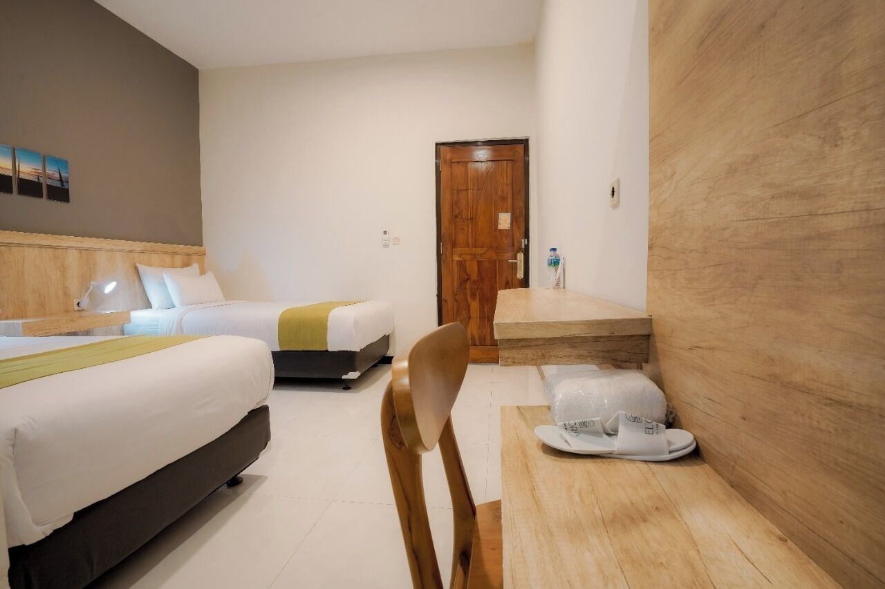 A hotel room with two beds, a wooden headboard, a small table with a chair, and a door.