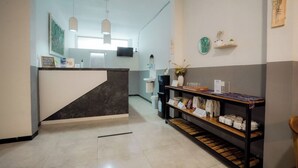 Una zona de recepción con mostrador de mármol, estante de madera con bolsos, un reloj y un televisor en la pared.