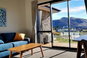 Une pièce avec un canapé, une table, une grande fenêtre donnant sur la montagne et un mur en pierre.