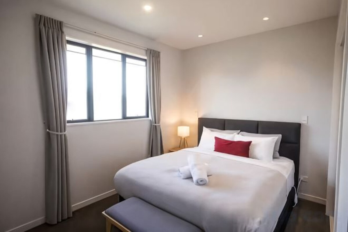 Een hotelkamer met een bed, een bankje, een nachtkastje en een raam met gordijnen.