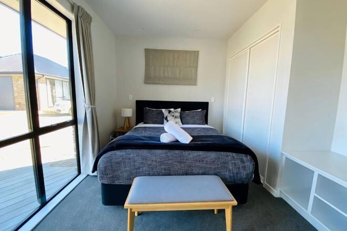 Un dormitorio con cama, un banco, un gato y una ventana.