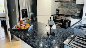 A modern kitchen with a black granite countertop, stainless steel appliances, and a built-in oven. - Luxury 4 bed House Sleeps 8, Enjoy in Comfort (Bridgend)