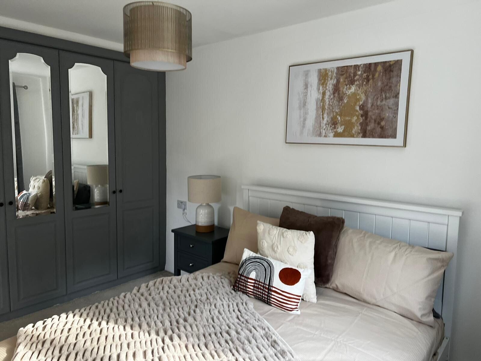 A bedroom with a bed, bedside table, lamp, and a painting on the wall.