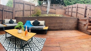 A wooden deck with outdoor seating, including sofas and a table with a bottle and glass. - Luxury 4 bed House Sleeps 8, Enjoy in Comfort (Bridgend)