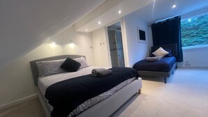 A modern bedroom with a large bed, a smaller bed, and a window with a view of greenery. - Luxury 4 bed House Sleeps 8, Enjoy in Comfort (Bridgend)