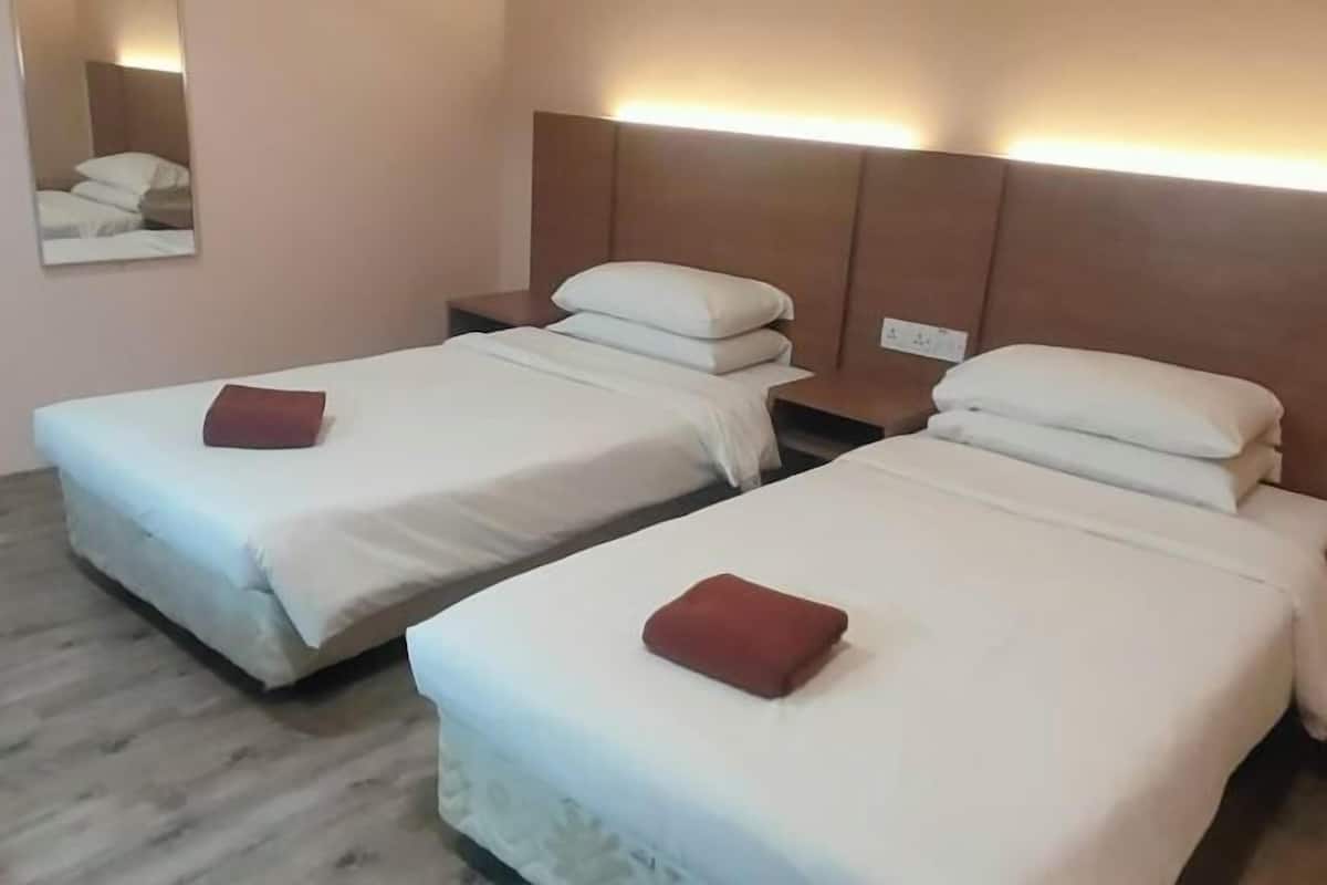 Habitació d'hotel amb dos llits, cada un amb un coixí i un coixí decoratiu vermell.