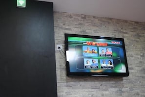 A flat-screen TV mounted on a brick wall, displaying a news channel. - Walk Inn (Miri)