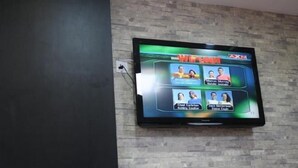 A flat-screen TV mounted on a brick wall, displaying a game show.