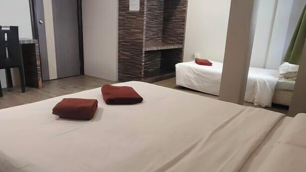 Une chambre d’hôtel avec un lit, deux coussins rouges, un canapé blanc, un mur en bois et une porte.