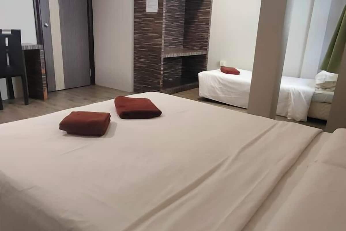 Habitació d'hotel amb un llit, dos coixins vermells, un sofà blanc, una paret de fusta i una porta.