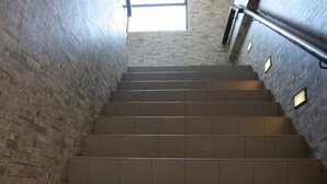 A staircase with a handrail, leading upwards, surrounded by brick walls.