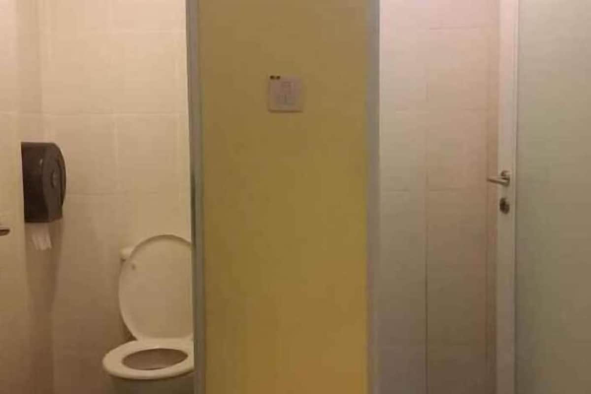 Un baño con inodoro, secamanos y pared amarilla.