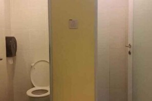 Un baño con inodoro, secamanos y pared amarilla.