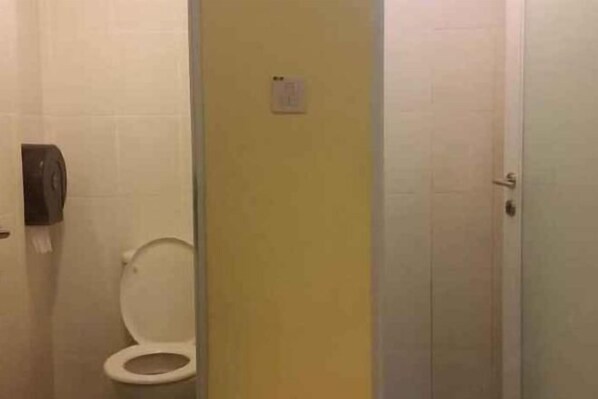A bathroom with a toilet, a hand dryer, and a yellow wall.