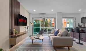 Sala de estar moderna com sofá, mesa de centro e TV na parede exibindo 'NETFLIX'.