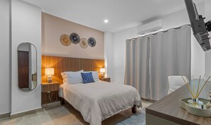 A hotel room with a bed, bedside lamps, a mirror, a wall-mounted air conditioner, and a desk with a diffuser.