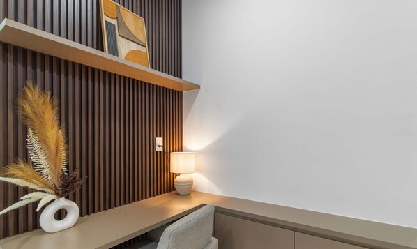 Un intérieur moderne avec un mur à lattes de bois, un vase blanc contenant des plumes d’herbe des pampas, une lampe et un canapé gris.