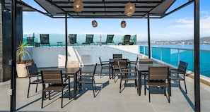 An outdoor terrace with chairs and tables, overlooking a body of water. - Risco - Downtown Bucerias, Rooftop Pool. (Bucerías)