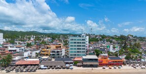 A coastal cityscape with a mix of modern and traditional buildings, a beach with umbrellas, and a clear sky.