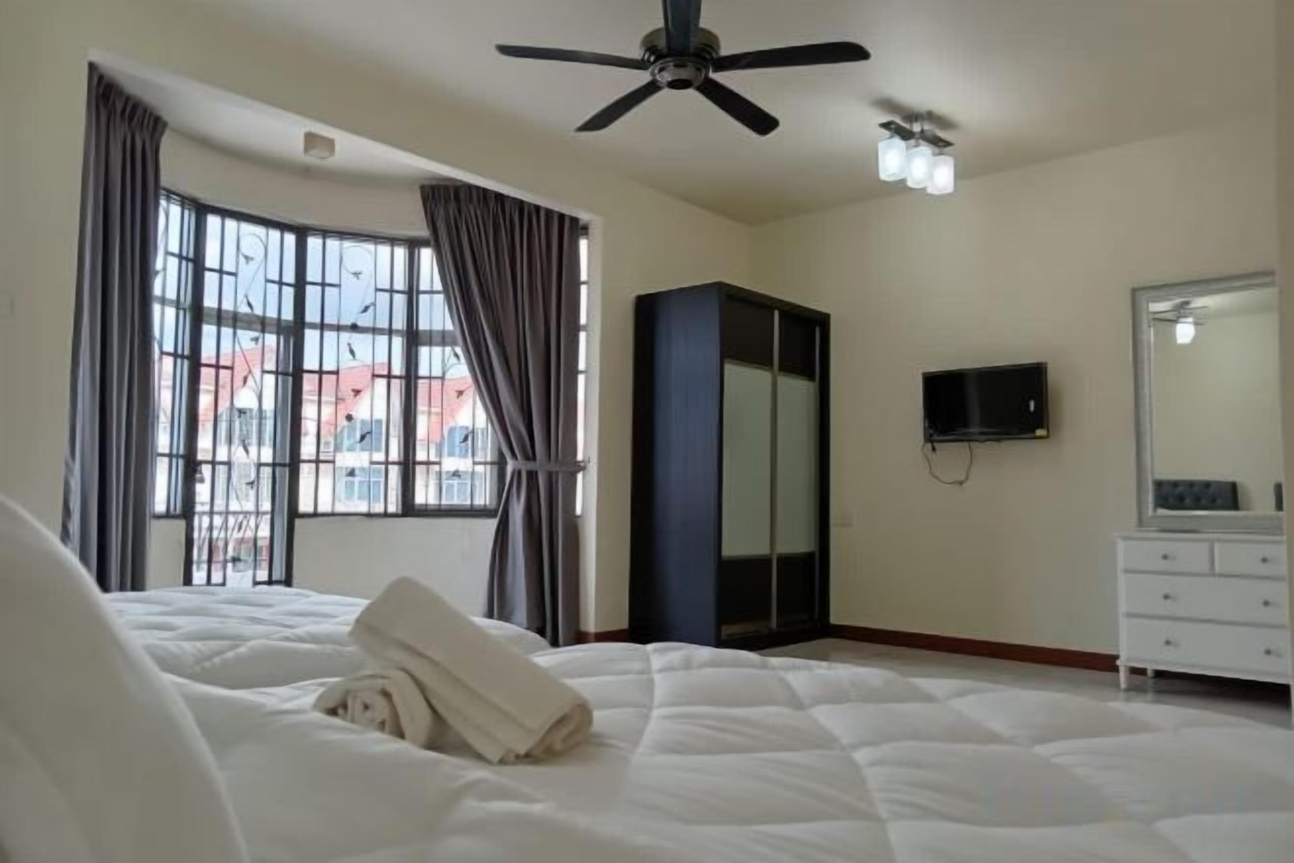 A hotel room with a bed, a ceiling fan, a TV, a wardrobe, and a window with curtains.