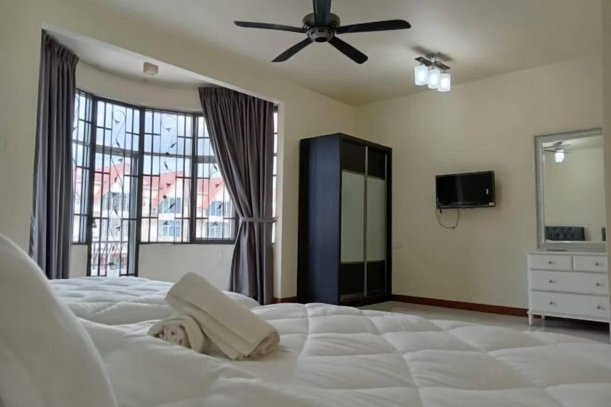 A hotel room with a bed, a ceiling fan, a TV, a wardrobe, and a window with curtains.