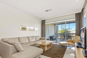 A modern living room with a sofa, coffee table, flat-screen TV, and a glass door leading outside.