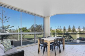 A balcony with a table and chairs, large windows, and a view of trees and buildings. - Bale Luxury Resort - Holiday Management (Kingscliff)