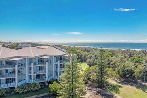 A multi-story building with a balcony, surrounded by trees and a view of the ocean.