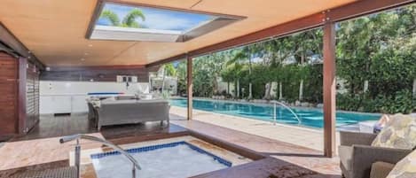 A modern indoor pool area with a glass ceiling, a hot tub, and a seating area overlooking a swimming pool.