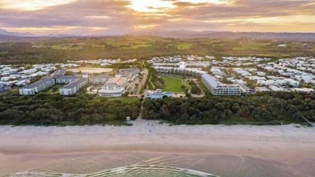 Luchtbeeld van een resort met meerdere gebouwen, een strand en een heldere lucht.