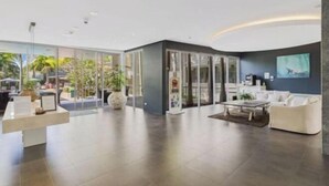Een moderne hotellobby met een receptiebalie, een zithoek en glazen deuren die naar buiten leiden.