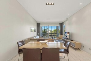 Un salon moderne comprenant un coin repas, de grandes fenêtres et un téléviseur à écran plat.