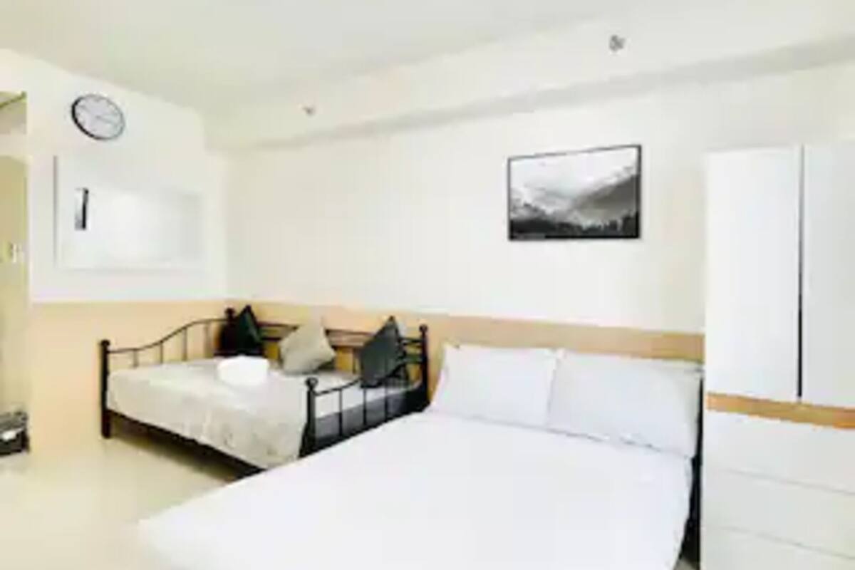 Un dormitorio con una cama grande, una mesita de noche, un armario, un reloj y un cuadro en la pared.