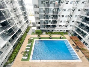 Un immeuble d’appartements moderne doté d’une piscine centrale, de nombreux balcons et d’un jardin bien entretenu.