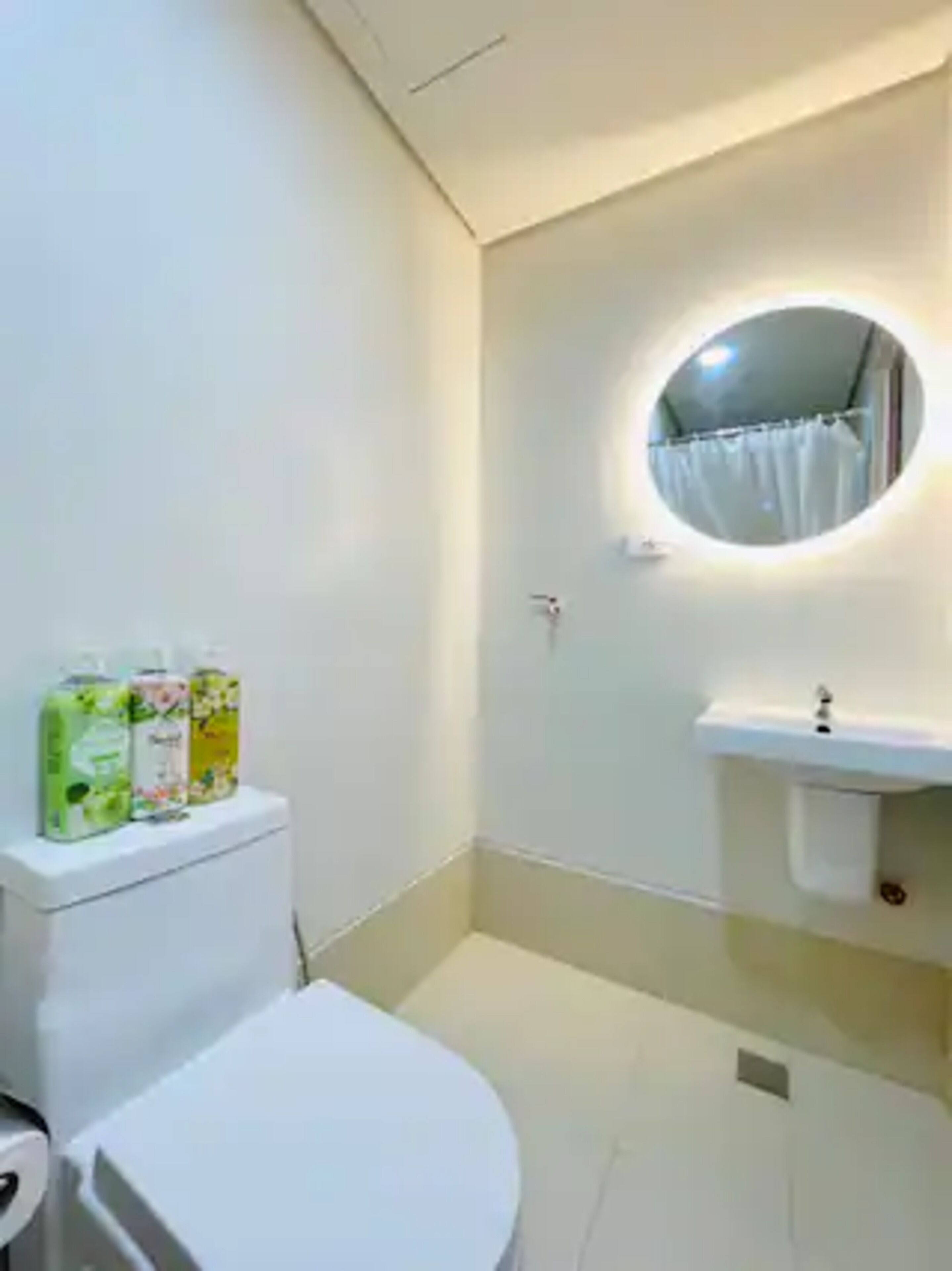 A small bathroom with a toilet, a sink, and a mirror. There are three toiletry products on the toilet tank.