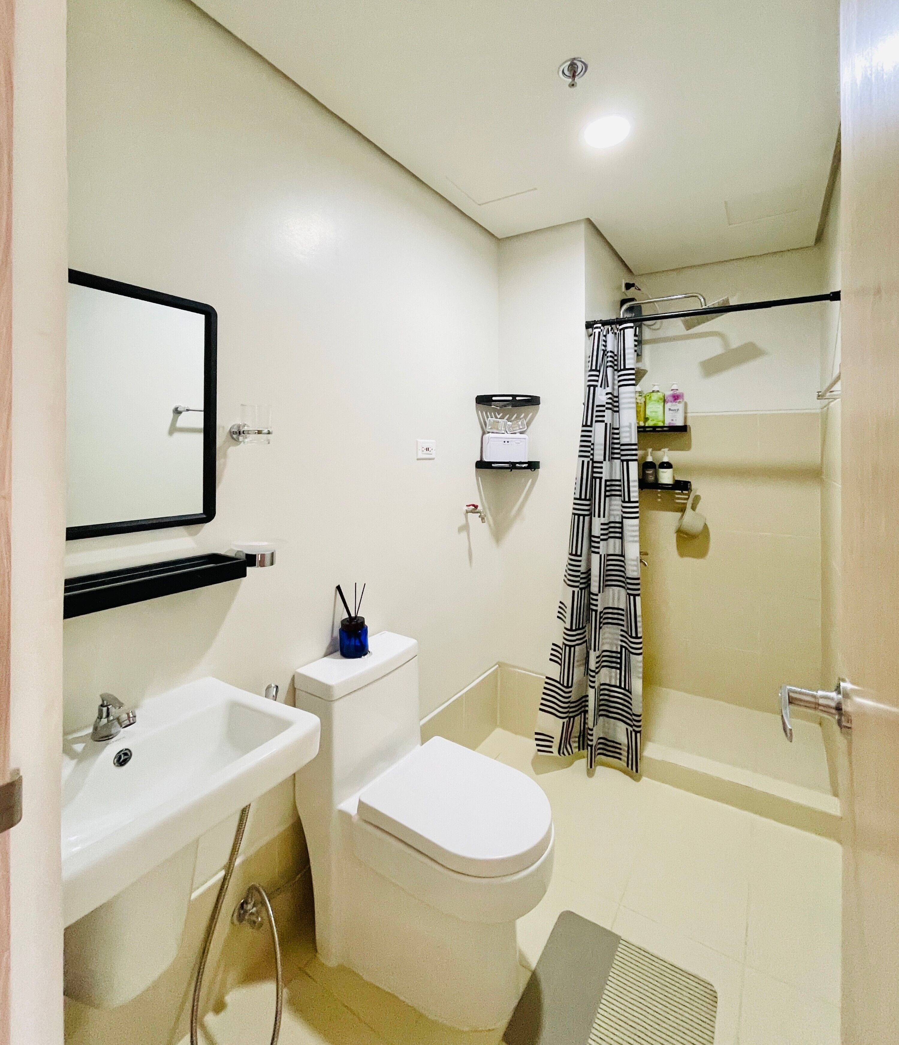 A bathroom with a sink, toilet, and bathtub. There is a shower curtain and a shelf with toiletries.