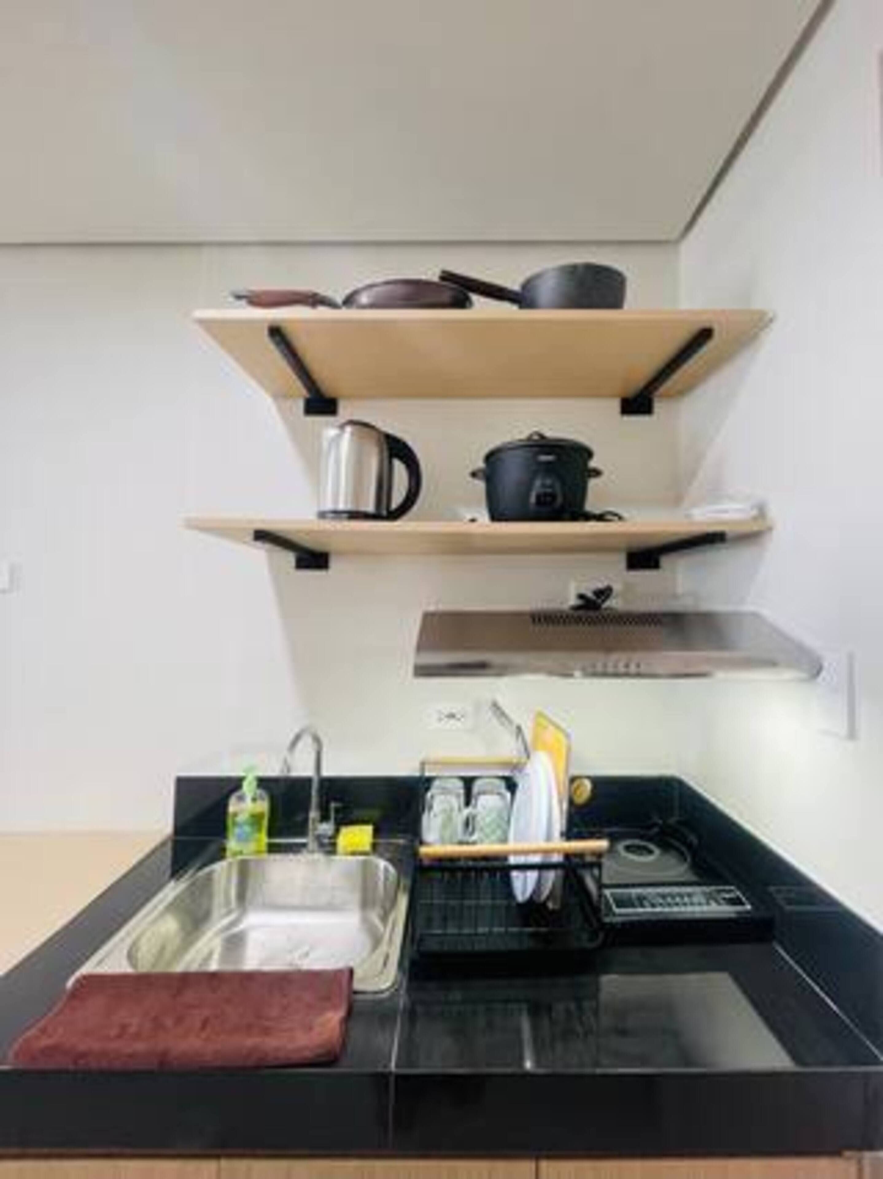 Eine Küche mit schwarzer Arbeitsplatte, einem Edelstahl-Spülbecken und Holzregalen, auf denen Küchenutensilien stehen.