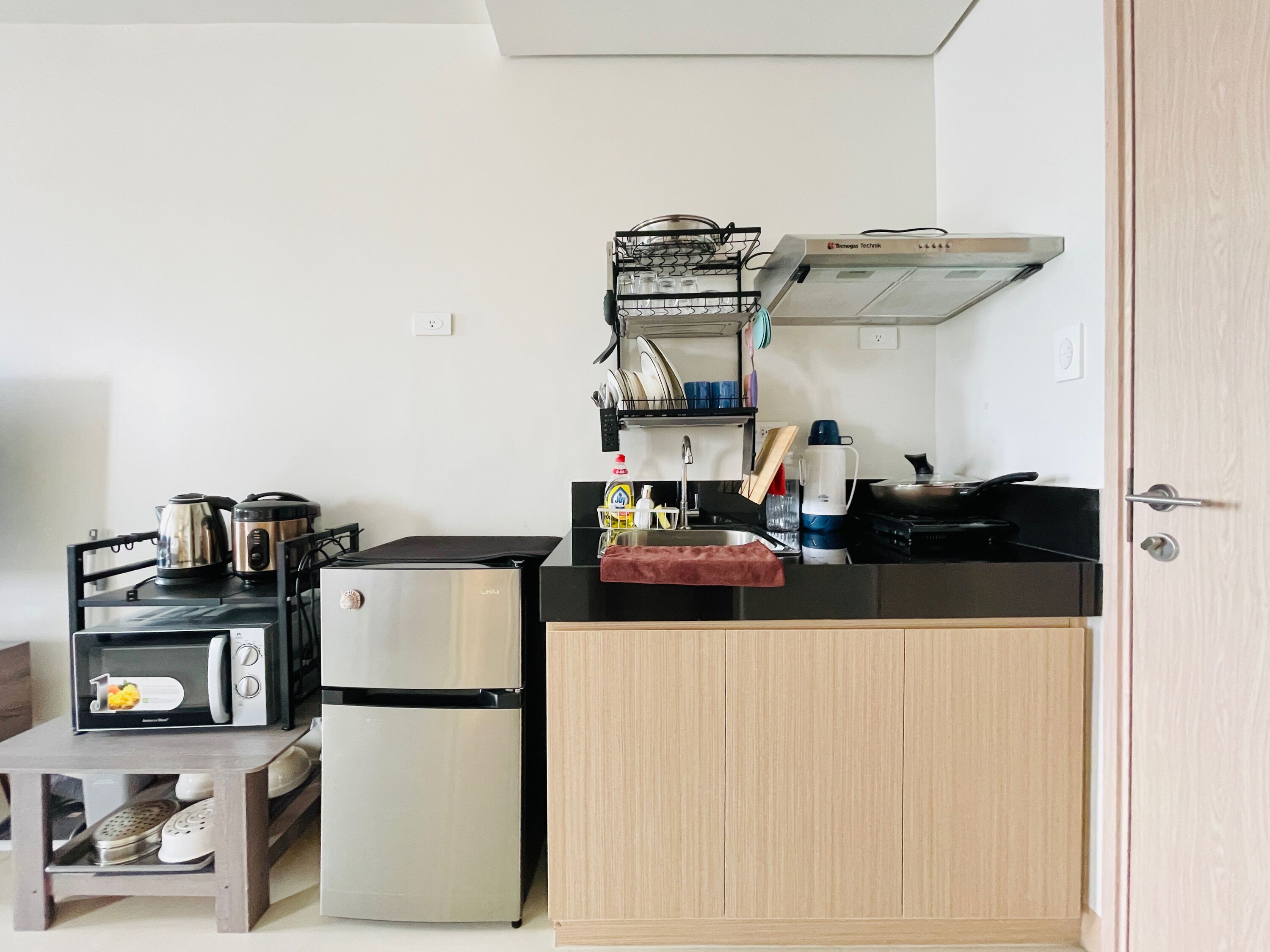 Una cocina compacta equipada con refrigerador, microondas, hervidor y una pequeña mesa de comedor.