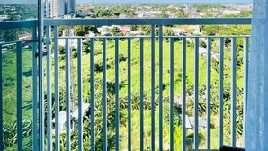 Un balcon doté d’une balustrade en métal, d’où l’on peut admirer un paysage urbain avec ses bâtiments et sa végétation.