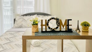 Une chambre à coucher bien rangée, avec un lit, une table de chevet ornée d’un petit objet décoratif portant l’inscription « HOME », une miniature de la Tour Eiffel et deux plantes en pot.