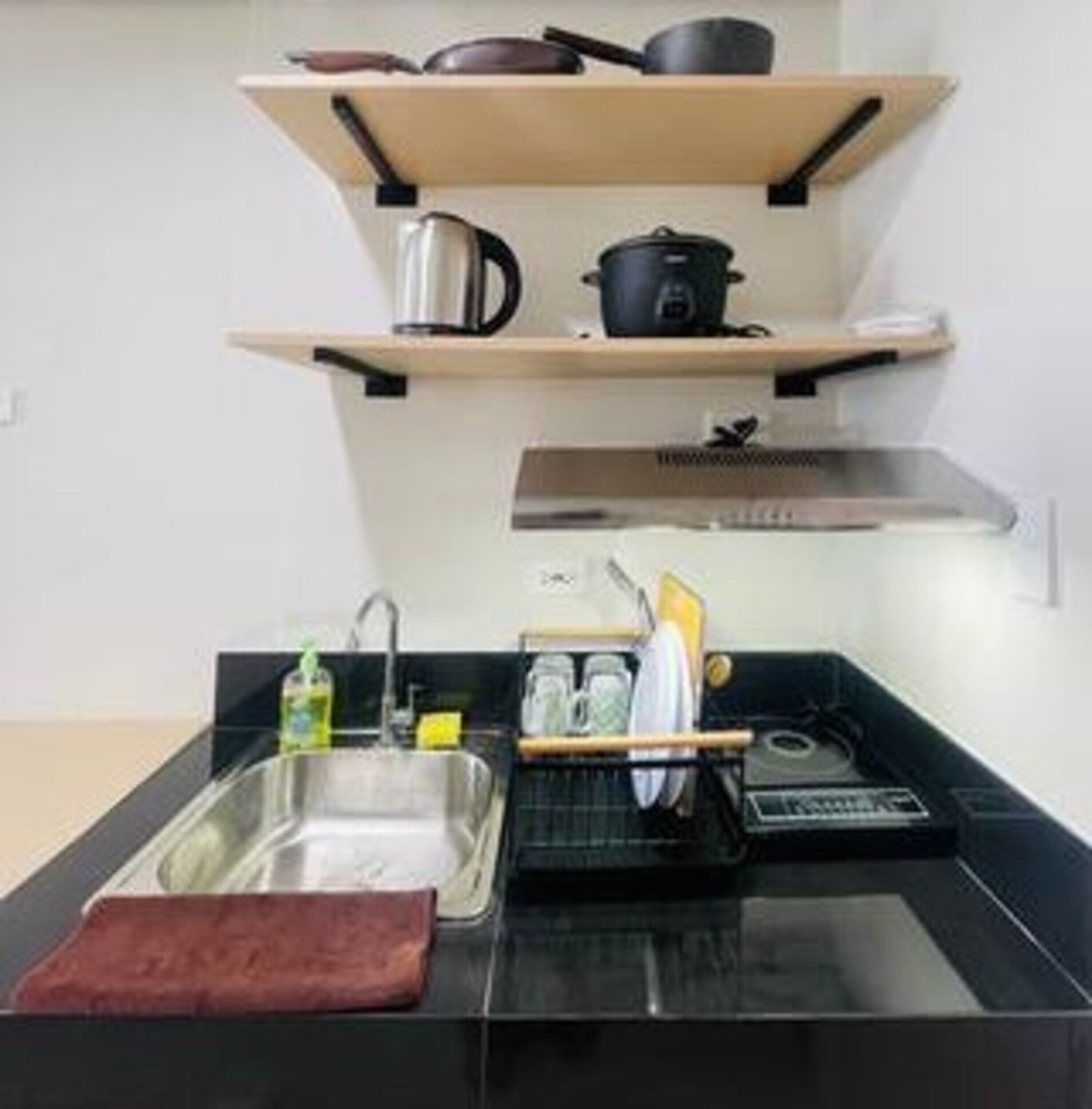 A kitchen with a black countertop, a stainless steel sink, a dish rack, and a red cutting board.