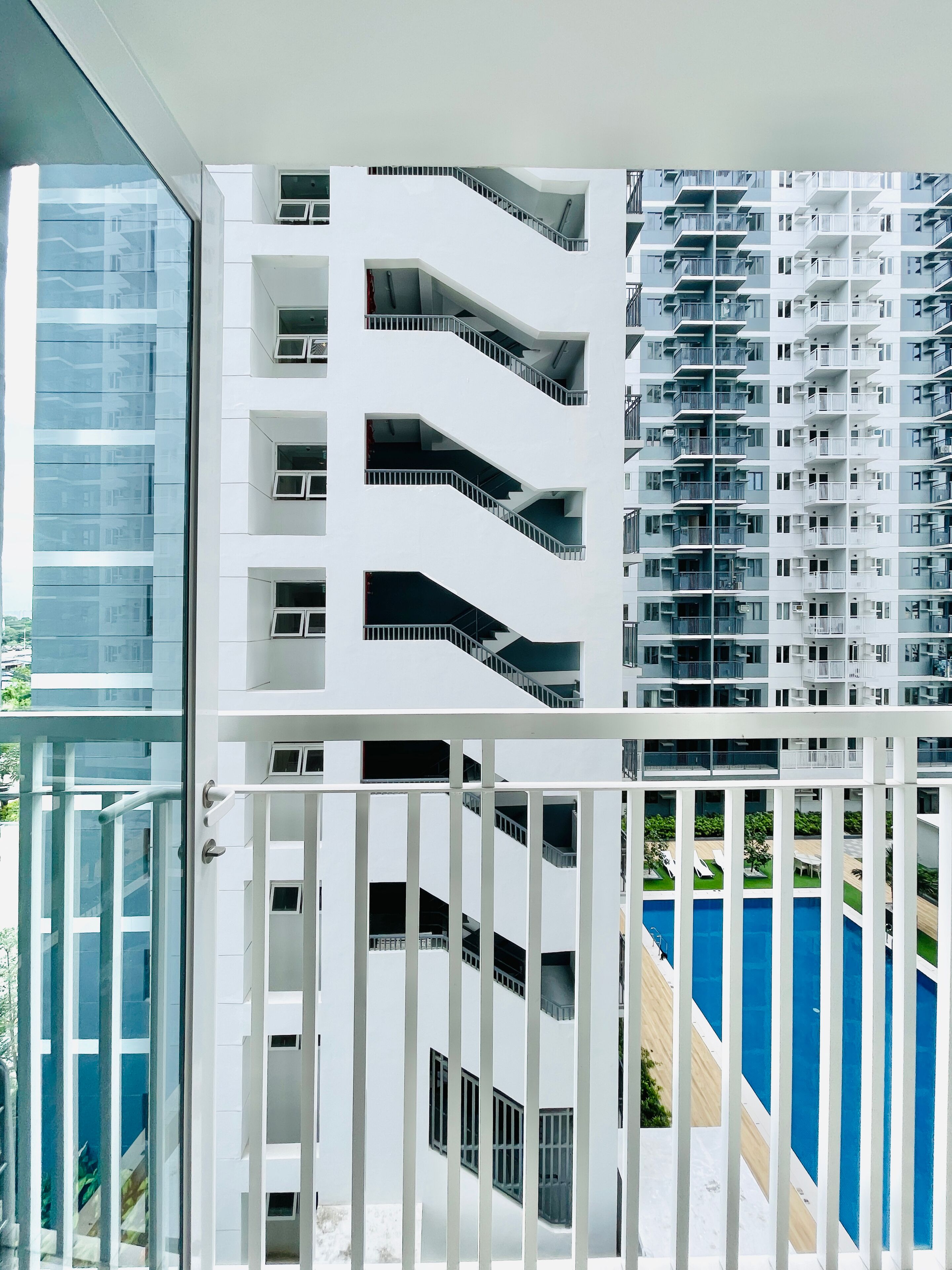 Un immeuble moderne à plusieurs étages, doté de balcons, d’une façade en verre et d’un espace piscine visible à travers une rambarde.