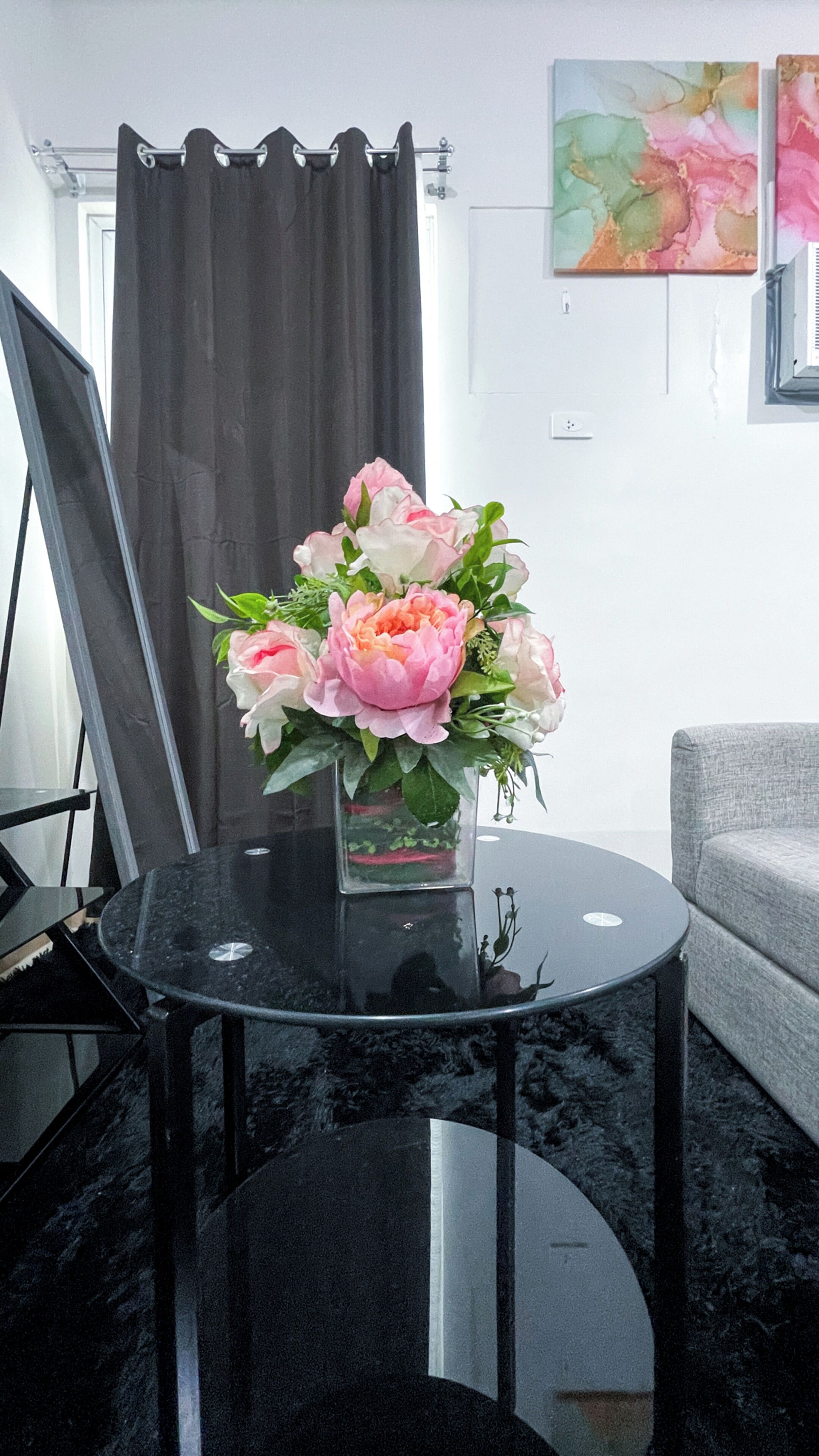 A room with a black round table, a grey sofa, a black curtain, and a framed painting on the wall.