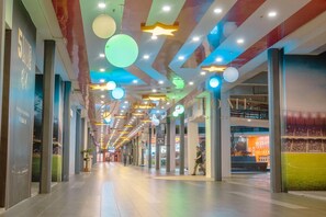 Een gang met een hoog plafond, ingebouwde verlichting en een muurschildering van een sportveld aan de rechterwand.