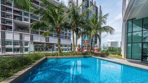 Um edifício moderno com piscina, palmeiras e um colorido parquinho.
